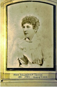  Sepia photograph of a young woman with short curly hair and wearing a frilly blouse. The photograph has a frame within its boundary. Physical description