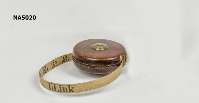 A tape measure on a reel contained in a leather circular case with a brass winding mechanism.