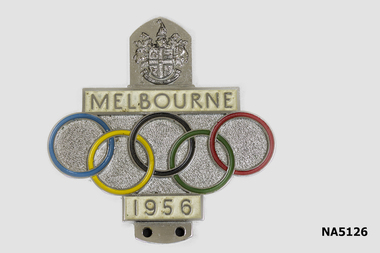 Car badge with 5 Olympic rings and 'Melbourne' across at the top and 1956 at the bottom of the rings.