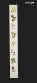 A long cotton material with eight embroidered flowers down the centre. Top has metal rod and chain and at the bottom is a metal rod