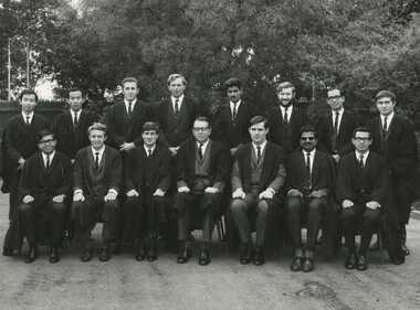Black and white photographs showing fourteen male tutors of International House and the Warden of International House Sam Dimmick dressed in suits and academic gowns. 
