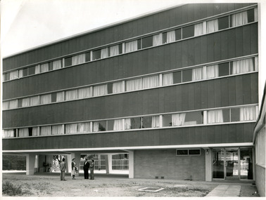 Black and white photograph of newly constructed Clunies Ross Wing at International House. Four people, 3 men and 1 woman, stand outside the building.