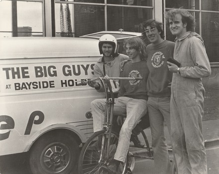 Photograph of 4 students posing with tricycle post-victory of race