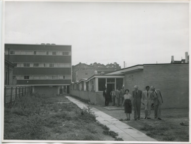 A women and three men standing in a row on the unmanicured lawn of a 1957 International House campus, a row of four men stand a short distance behind them
