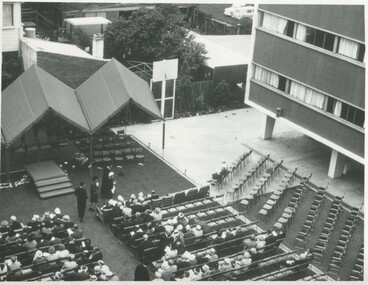 A birds eye view people sitting in rows of chairs in front of a podium, the rows furthest to the right are empty