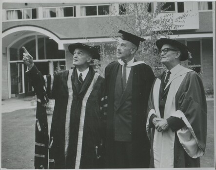 Three men in their 60s or 70s, outdoors on the International House campus in traditional Oxford gowns  