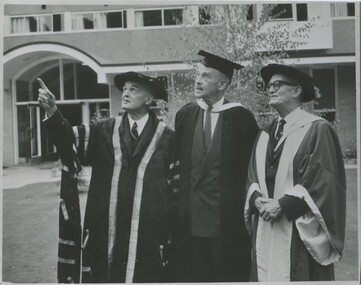 Three men in their 60s or 70s, outdoors on the International House campus in traditional Oxford gowns  