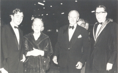 Four people (three men and one woman) stand in a row looking at the camera. They wear formal dress.