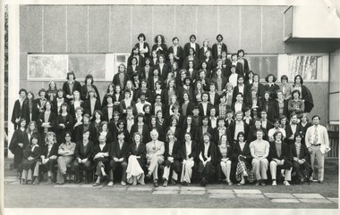 Large group photo of around 75 people dressed business casual with black robes on over their clothes. 