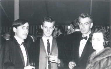 Three men and one woman in formal dress stand in a row, looking at the camera.
