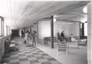 In the background two men in suits shake hands on the left, and two men and a woman sit chatting on the right