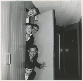 Five young male students peaking out from a doorframe making funny faces