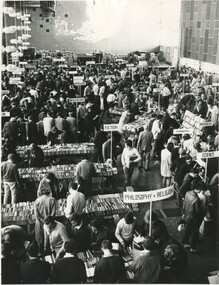 A photo from above of a book sale. A large room full of rows of books, records, and crowds of people. 