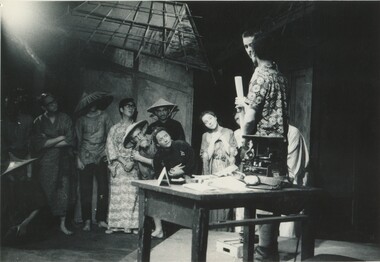 A stage made to look like a rural location in Japan with students wearing conical straw hats and kimonos. 