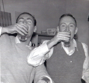 Two men face the camera, drinking from glasses 