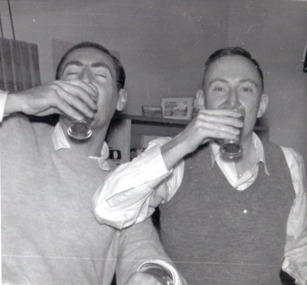 Two men face the camera, drinking from glasses 