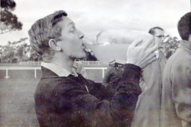 Young man in profile drinks from a large glass bottle filled with cloudy liquid