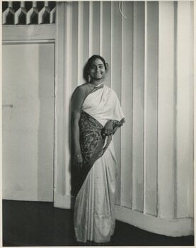 Woman standing in a sari in front of a white panelled wall and door. 