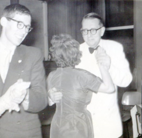 Two couples dancing, both men are visible and smiling, one woman has her back to the camera, and one is out of shot