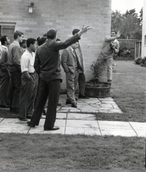 Group of male students in a group outside. Two students at the front of the group gesture to the right animatedly.