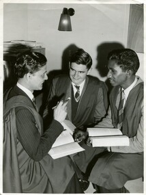 Three boys, in oxford robes, sitting in a circle. Two of them have open books on their laps, they are chatting excitedly. 