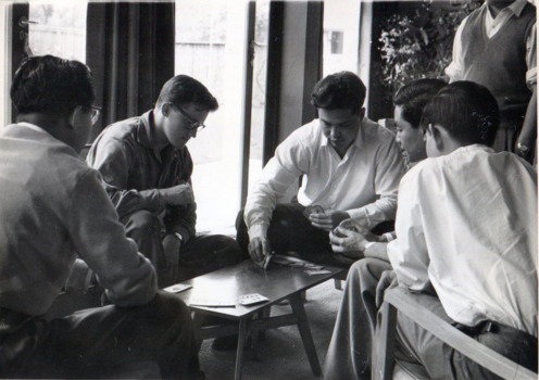 Five men sit around a low wooden table playing a card game.