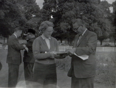 Woman and man hold an unidentified item from either side. They are outside in a park area.