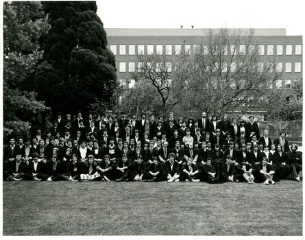 Photo of around 50 students and staff in suits and Oxford robes outdoors