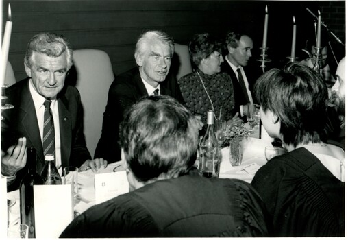 Well-dressed men and women of various ages sitting and chatting at a long table for dinner. 