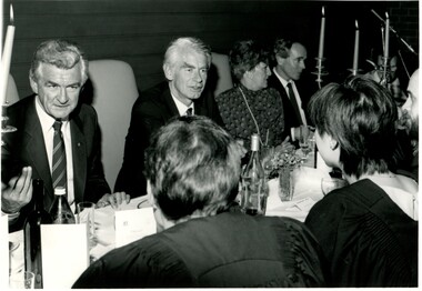 Well-dressed men and women of various ages sitting and chatting at a long table for dinner. 