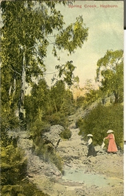 Two women in long dresses and hats walk along a stony creek