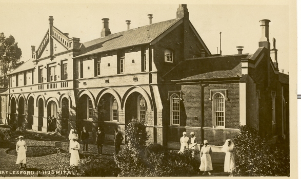 Three men and six nurses stand in front of a double storey hospital