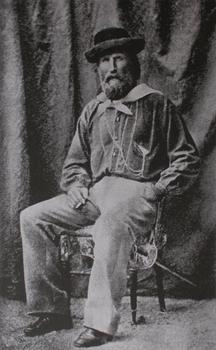 A man in a hat sits on a chair smoking a cigar.