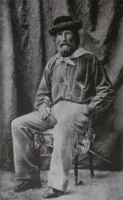 A man in a hat sits on a chair smoking a cigar.
