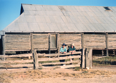 Two women stand at a post and rail fence