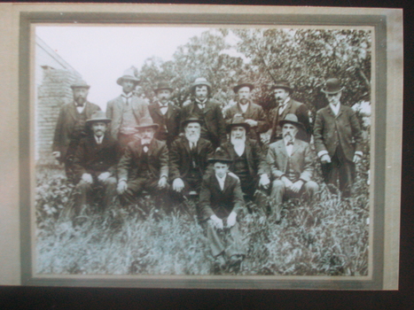 Thirteen men in hats sit for a group photograph