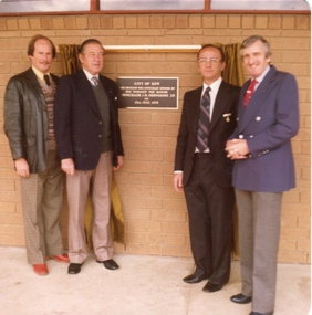 Four men outside a plaque