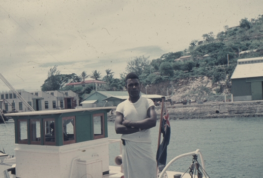 Sem on the wharf at Port Moresby with houses and boat with Australian flag in the background.