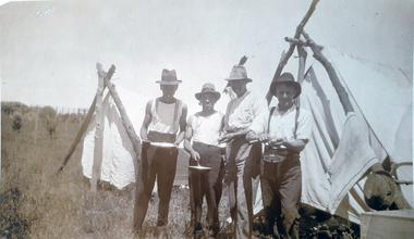 Four men stand in front of 2 tents