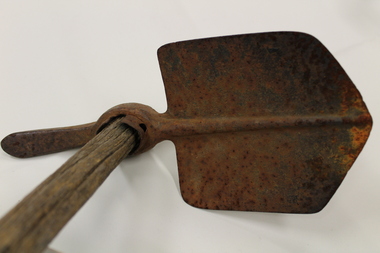 Small metal shovel with a pick spike on the other end, used for digging trenches and latrines. It also has a small wooden handle.