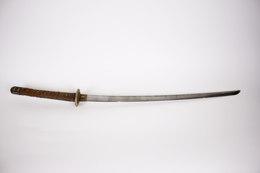 Image of a Japanese sword with a plaited cloth hilt. The hilt is to the left with the blade pointing to the right.
