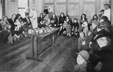 Ladies, children and medical staff in the Ante-Natal Clinic waiting room in the Melbourne District Nursing Society After-Care Home.
