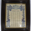 Black wooden, glass fronted frame of printed poster. White background with blue text. Illustrated columns with flags and crowns atop and women holding wreaths on sides.Five columns of names in small black priint. 