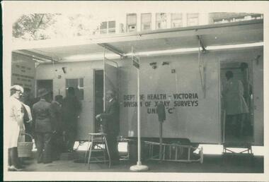 Photograph, Mobile chest x-ray clinic van on site on Melbourne street, showing individuals queuing to undertake screening for tuberculosis. Photo is from a photograph album circa 1962