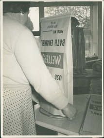 Photograph, Photo, taken for display purposes, by the Australian Institute of Engineers Exhibition 1960, of a women flaring a heavy duty Metters paper garbage bag, and adding a plastic bag insert, before adding the bag to a stack - Mont Park Occupational Therapy Unit