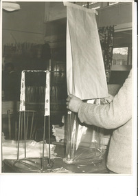 Photograph, Photo taken for display purposes by the Australian Institute of Engineers (AIE) Exhibition 1960 of a women fitting a heavy duty Metters paper garbage bag with a plastic liner, before adding the bag to a stack - Mont Park Occupational Therapy Unit