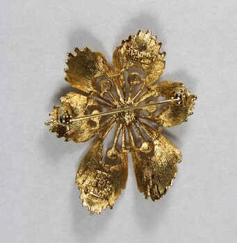 Back of a gold-toned metal brooch with one large central faux pearl surrounded by six smaller faux pearls.