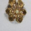 Front of a gold-toned metal brooch with one large central faux pearl surrounded by six smaller faux pearls, with a 5 cm black and white scale.