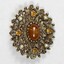 Front of an oval brooch from the Sarah Coventry jewellery range, with a central brown faux stone surrounded by four small faux pearls inlays and four small circular brown faceted glass inlays.