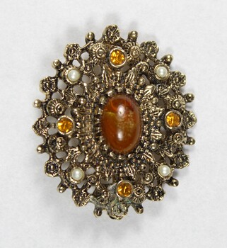 Front of an oval brooch from the Sarah Coventry jewellery range, with a central brown faux stone surrounded by four small faux pearls inlays and four small circular brown faceted glass inlays.
